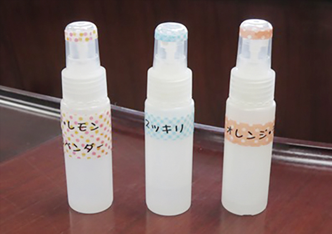 写真:3本のスプレー式容器にはスッキリ、オレンジ、などのアロマの種類を示すシールが貼られている。
